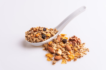 Granola or muesli with nuts and rasins in a white spoon on a white background, angle view, soft light