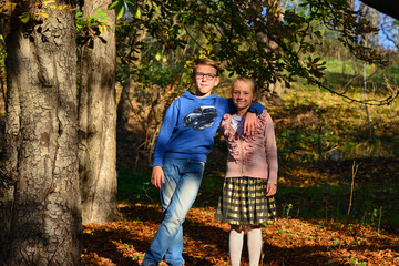 Fototapeta premium A boy with a girl are embracing in the forest on dry leaves on a summer evening, brother and sister in nature.