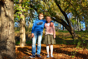 Fototapeta premium A boy with a girl are embracing in the forest on dry leaves on a summer evening, brother and sister in nature.