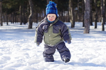 Fototapeta na wymiar toddler boy walks in the snow in winter park