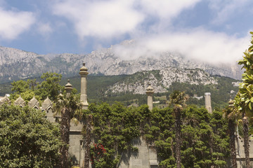 Obraz premium A wall with Moorish turrets, overgrown with lush greenery and a view of the peaks of AI-Petri in the clouds.Crimea.