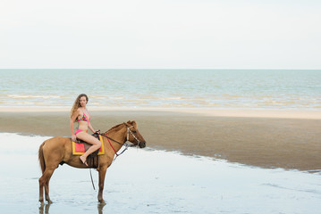 Fototapeta na wymiar Pretty young lady riding a horse on the beach background of the sea