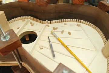 Luthier gluing parts harmonica structure top with brush and tweezers of a classical guitar