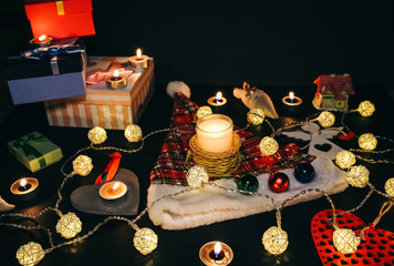 Candles burning among beautiful Christmas lights and garland. New Year festive background. Presents, gifts, greeting postcard for winter holidays.
