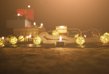 Candles burning among beautiful Christmas lights and garland. New Year festive background. Presents, gifts, greeting postcard for winter holidays.