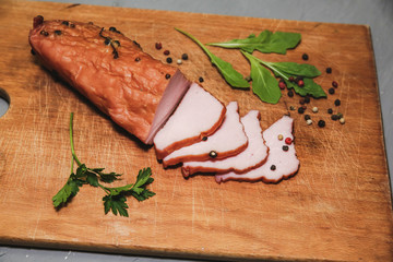 Tasty ham lying on the wooden panel plank. Meat with green leaves spinach. Food photo with pepper spices.
