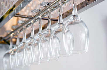 Empty tall wine glasses hanging in shelf above a bar rack in restaurant