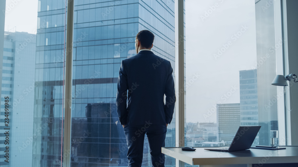 Wall mural back view of the thoughtful businessman wearing a suit standing in his office, hands in pockets and 