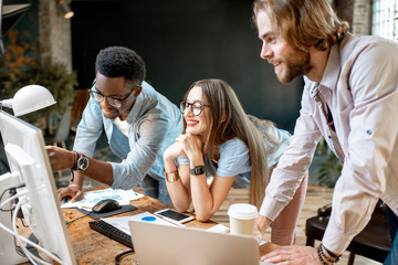 Group of young multi ethnicity coworkers dressed casually working together focused on the computer monitor indoors