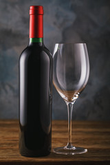 Bottle of red wine and empty glass close-up on wooden table