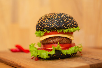 Black burger on board on dark wooden table background. Fast food.