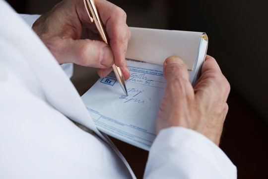 Closeup Of A Doctor Writing A Prescription On A Blue Prescription Pad.