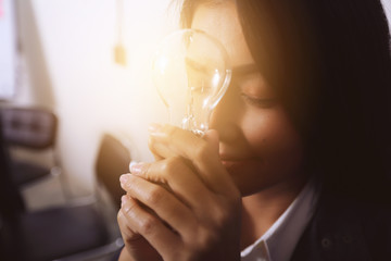 Business woman sitting holding a light bulb and closed eyes.