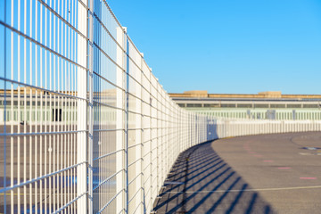 Fototapeta premium Diminishing perspective view of tall white grid metal curved fence on old landing field in former military airport in Berlin, Germany. 