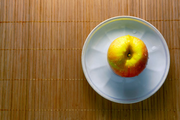 A fresh red and yellow wet apple on a plate