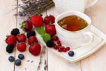 Herbal tea with lavender and mint with fresh strawberries, blackberries and blueberries on a white wooden table. Berry tea with fresh strawberries, blackberries and lavender herb. White porcelain 