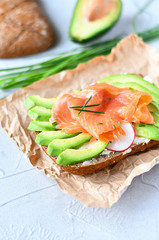 sandwich with avocado and salmon on a light background, green onions and gluten-free grain bread, radishes and tomatoes. concept diet food, vegetarian, copy space