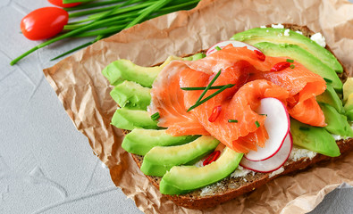 sandwich with avocado and salmon on a light background, green onions and gluten-free grain bread, radishes and tomatoes. concept diet food, vegetarian, copy space