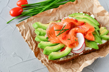 sandwich with avocado and salmon on a light background, green onions and gluten-free grain bread, radishes and tomatoes. concept diet food, vegetarian, copy space