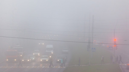 cars and people in the fog on a city street