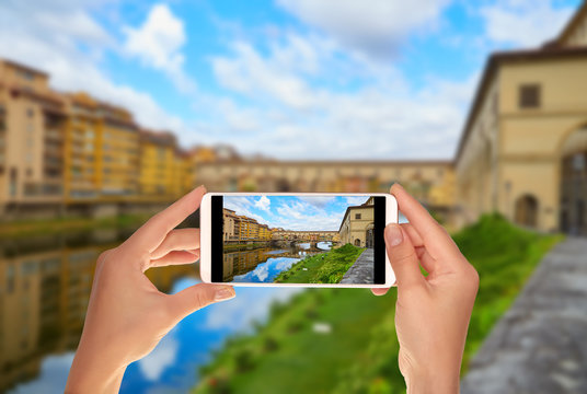 A tourist is taking a photo of Ponte Vecchio Bridge in a summer sunny day without people on a mobile phone