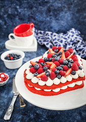 Delicious homemade heart shaped red velvet cake decorated with cream and fresh berries