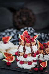 Delicious Pavlova meringue cakes decorated with chocolate cream, fresh figs and raspberries on dark background