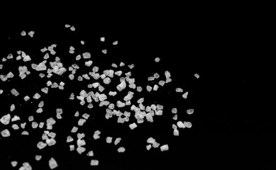 Spilled white sea salt on a black background. Transparent pebbles on a black background