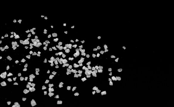 Spilled white sea salt on a black background. Transparent pebbles on a black background