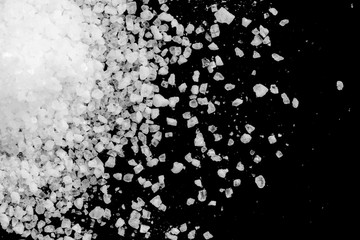 Spilled white sea salt on a black background. Transparent pebbles on a black background