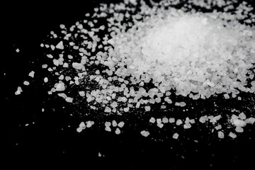 Spilled white sea salt on a black background. Transparent pebbles on a black background
