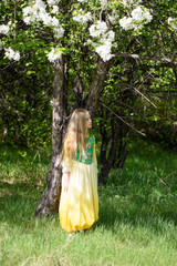 Blond young girl posing in a yellow green dress standing near apple trees