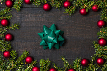 Dark rustic wooden table background with gift bow and Christmas decoration -  fir and red ornament frame. Top view with free space for copy text
