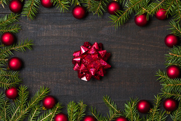 Dark rustic wooden table background with gift bow and Christmas decoration -  fir and red ornament frame. Top view with free space for copy text