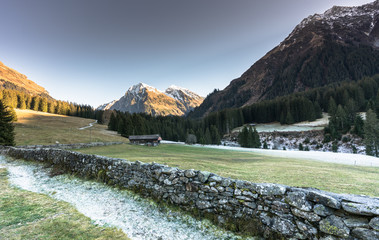 mountain landscape and valley with forest and snow-capped mountain peaks and an old rock wall with wooden huts and chalets behind