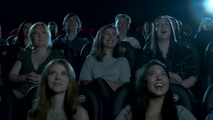 Young cinema audience watching a comedy movie, smiling and laughing.