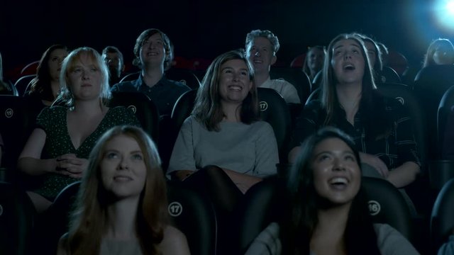 Young cinema audience watching a comedy movie, smiling and laughing.