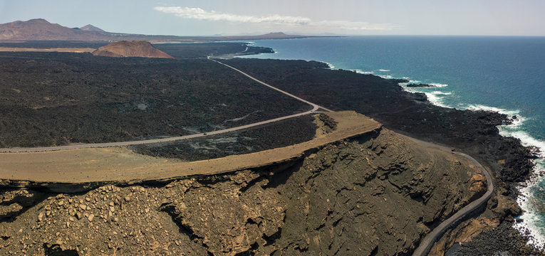 Vista aerea di rilievi, vulcani e campi di lava nell&rsquo;isola di Lanzarote, isole Canarie, Spagna. Coste frastagliate e strada che costeggia il mare