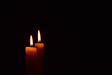 Yellow light candle burning brightly in the black background.