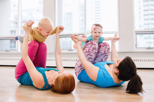 Group of two young women with children doing workout in gym class to loose baby weight. Child-friendly fitness for mothers with kids. Lifestyle concept of family activity for moms.