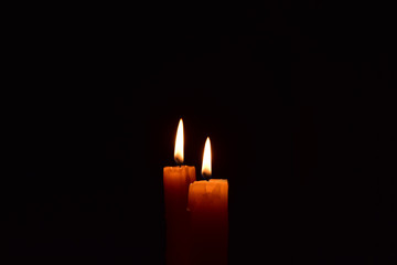 Yellow light candle burning brightly in the black background.