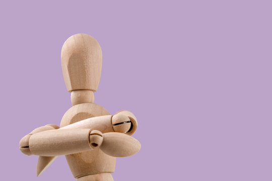 Wooden dummy holds two hands crossed in judgemental pose light violet background
