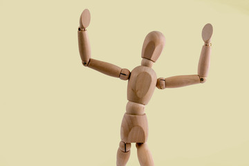 Wooden dummy holds two hands in air on light yellow background