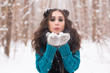 Christmas, holidays and season concept - Young happy brunette woman blowing snow in the winter nature