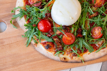 Close up of a pizza on a wooden board with cherry tomatoes, arugula, and cheese