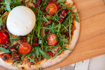 Close up of a pizza on a wooden board with cherry tomatoes, arugula, and cheese