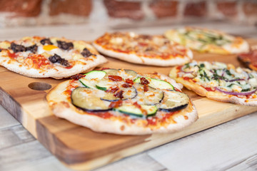 five pizzas on a wooden board with focus in vegetable pizza