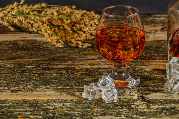 A glass of whiskey with ice or brandy and a square carafe on an old woody background. Whiskey with...