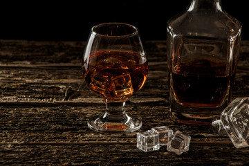 Whiskey with ice or brandy in a glass and a square carafe on an old wooden background. Whiskey with...