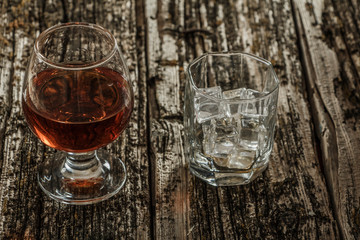 Whiskey with ice or brandy in a glass and a square carafe on an old wooden background. Whiskey with...